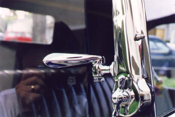 This close-up shows the earlier type safety glass marking. It is a scaled down (smaller) version of windshield markings. The original vacuum hose is cloth reinforced and has a cloth impression on the exterior. Like the terne finish vacuum tubing used elsewhere, the chromed tube on the stanchion has a lengthwise seam from the wrapped construction. The bright reflections tend to hide the distinct seam, but it can be seen just above the hose in this photo. The windshield and stanchion hinges used a small cadmium plated flat washer under the wingnuts.