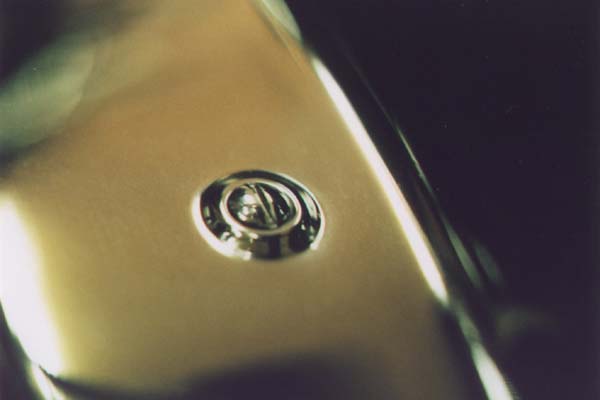 This is a close-up of a front fender to frame screw. Like nearly all original oval head machine screws, the slot is cut so the ends are even with the edges of the screw head. Modern oval head screws are slotted deeper at the ends.